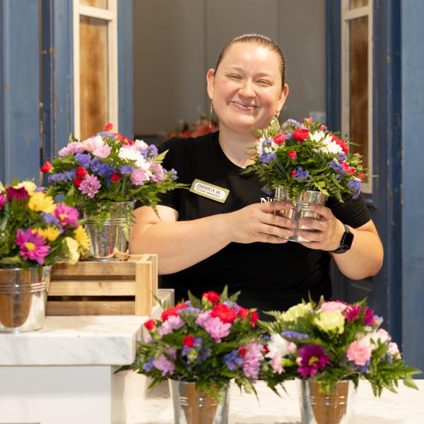 Floral Manager Danica M. holding an arrangement of flowers in store next to other similar floral arrangements