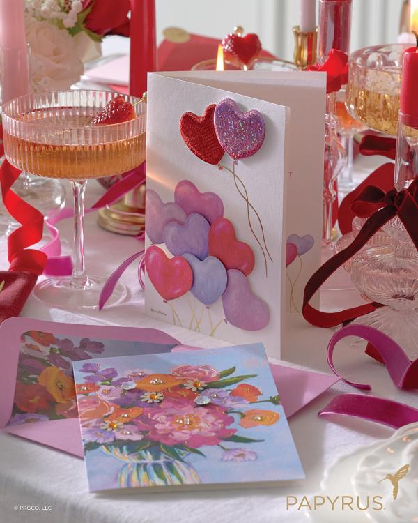 Papyrus Valentine's Day cards on a table with glasses of fruity cocktails, candles, and ribbons