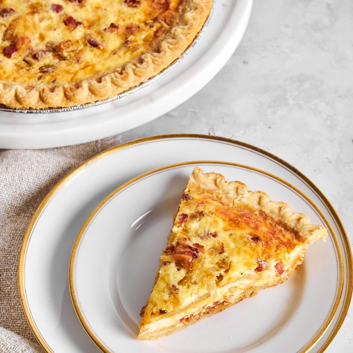 Slice of Bacon Apple Cheddar Quiche on two plates next to whole quiche