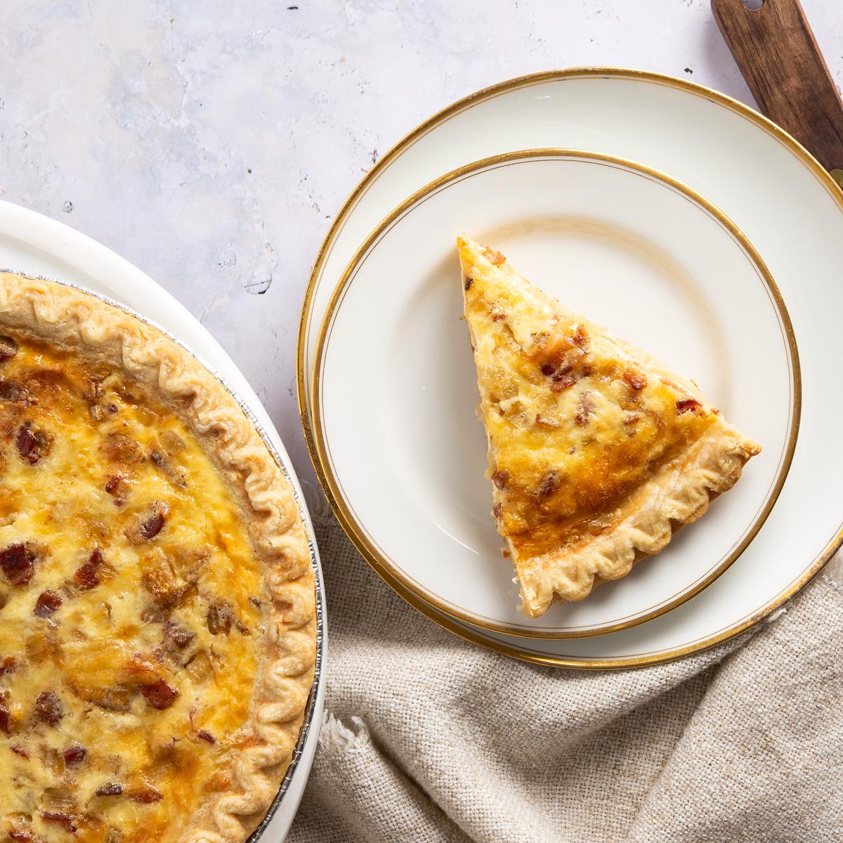 Slice of Bacon Apple Cheddar Quiche on two plates next to whole quiche