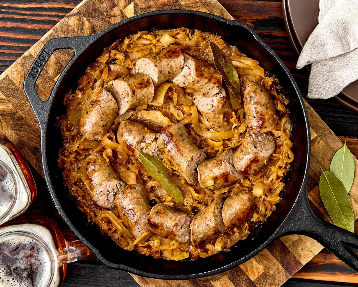 Sliced fresh to market beer and bratwurst sausages simmered with caramelized onions, sauerkraut and bay leaves in a cast iron skillet, served with mugs of beer alongside.
