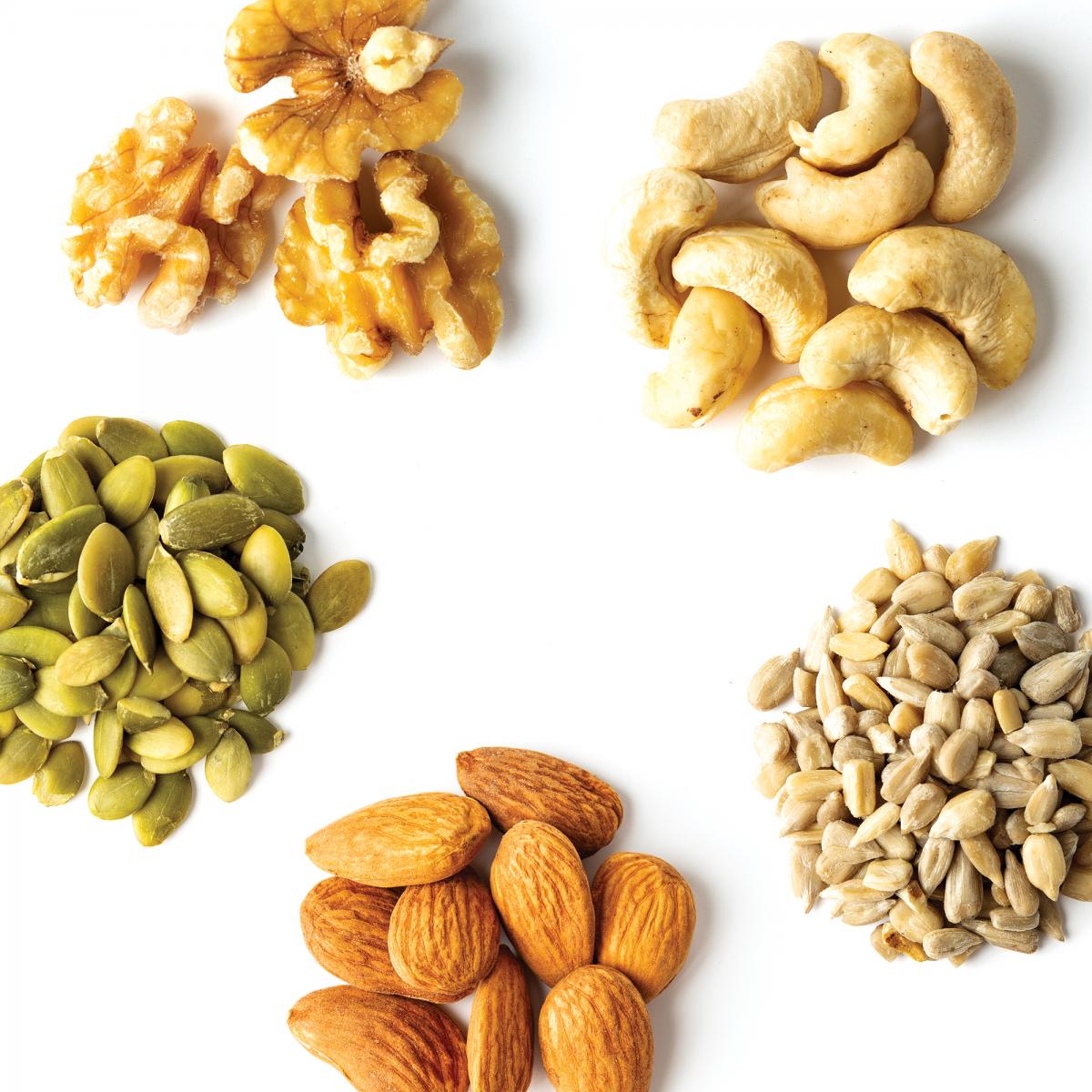 Five small piles of assorted nuts and seeds: walnuts, cashews, sunflower seeds, almonds, and pepitas