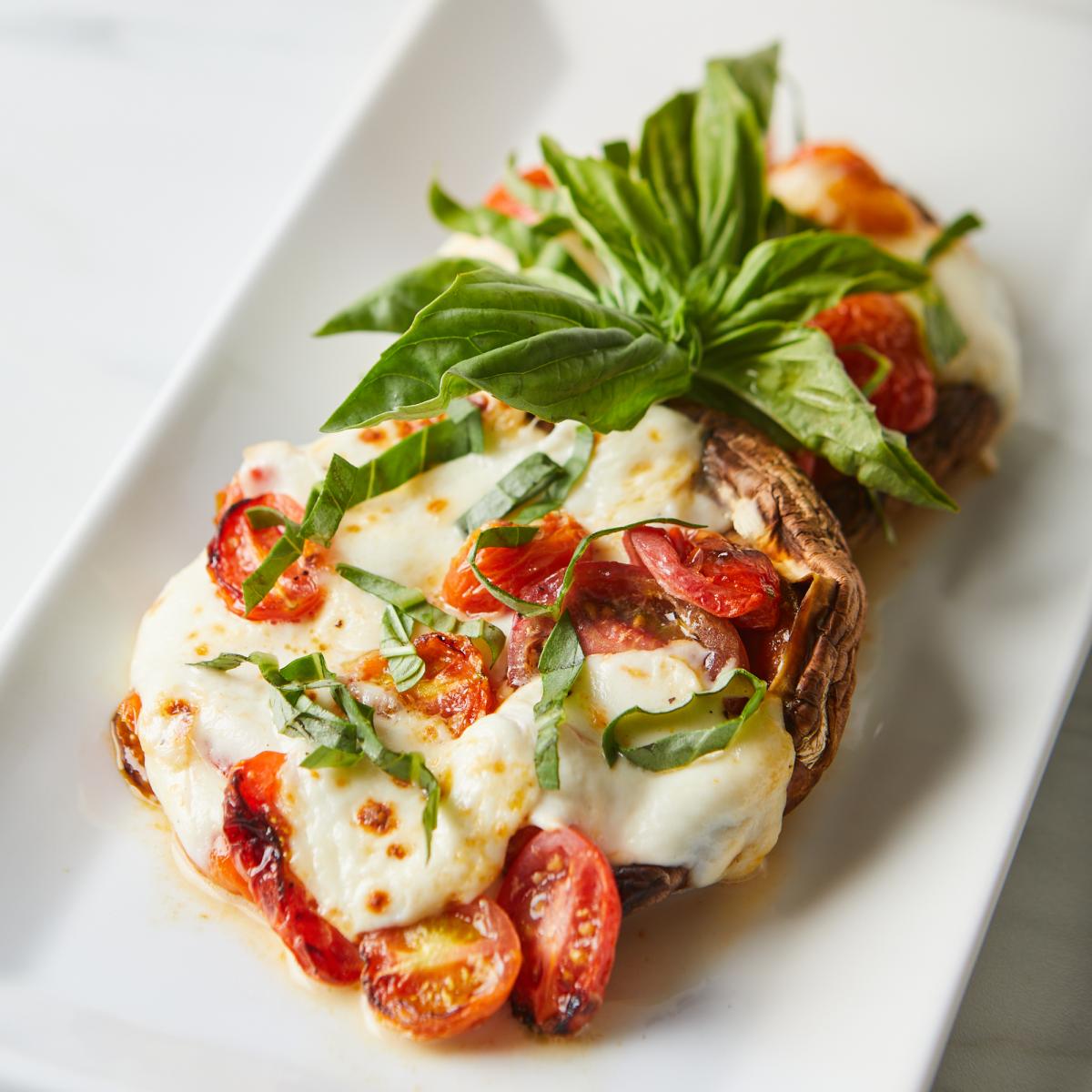 Two caprese-stuffed portobello mushrooms on a white serving dish