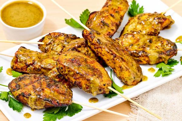 Chicken satay skewers on a plate with herbs next to a small bowl of sauce