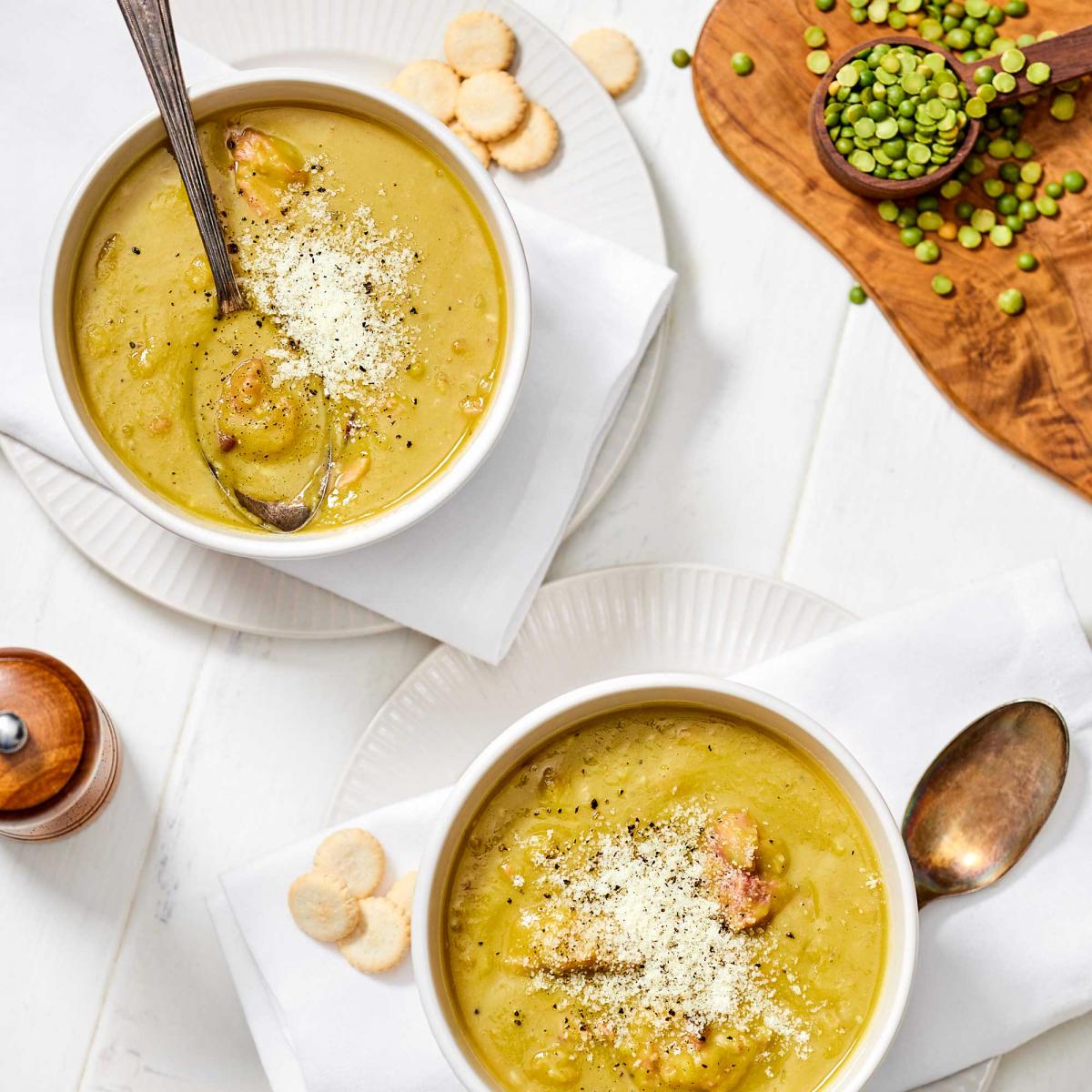 Classic Split Pea Soup in two bowls with round small crackers topped with dusted parmesan and some dried split peas spilled to the side