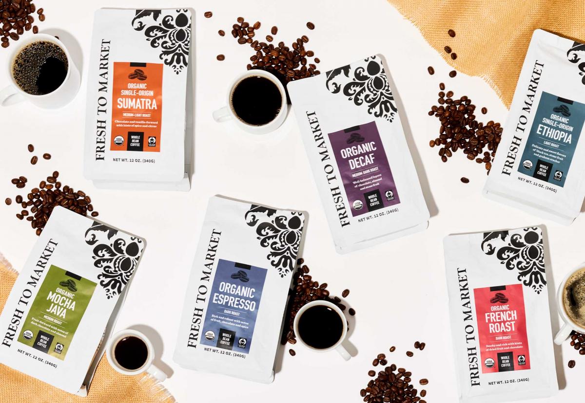 Six different bags of Fresh to Market Coffee surrounded by cups of coffee, coffee beans, and cloth napkins