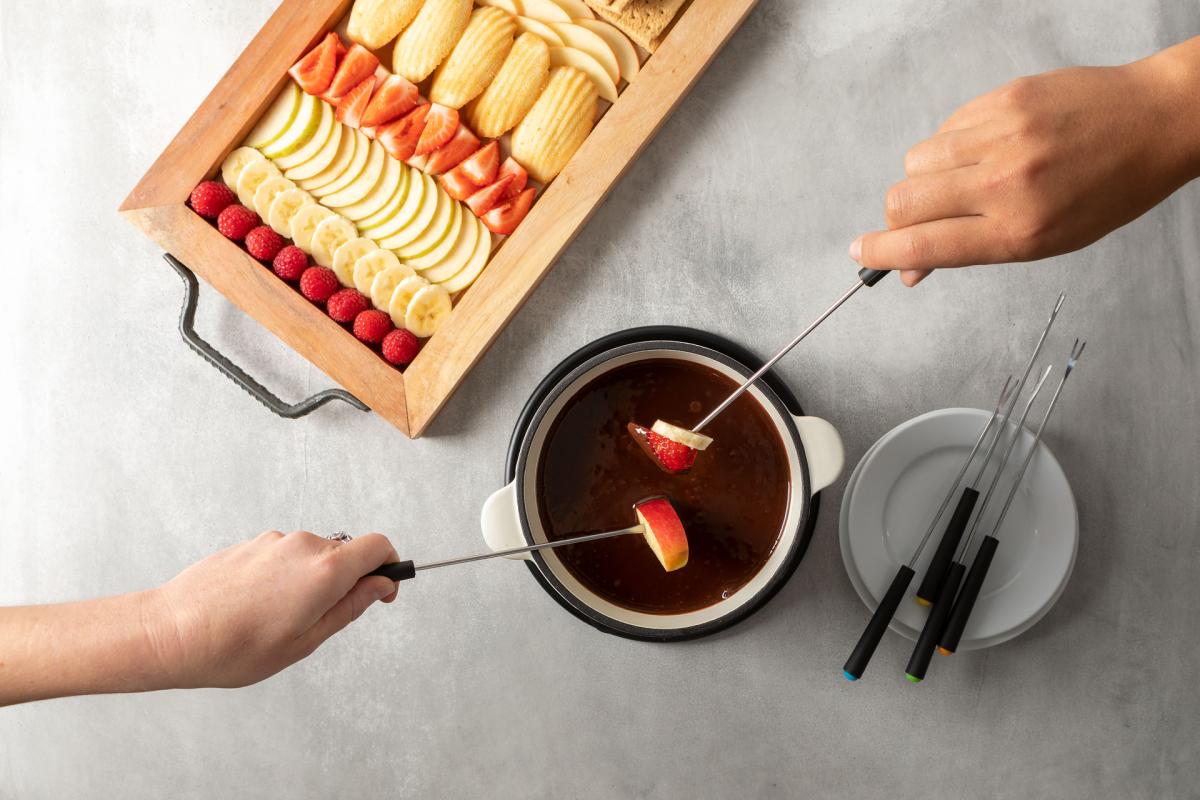 hands dipping sticks of fruit into chocolate fondue