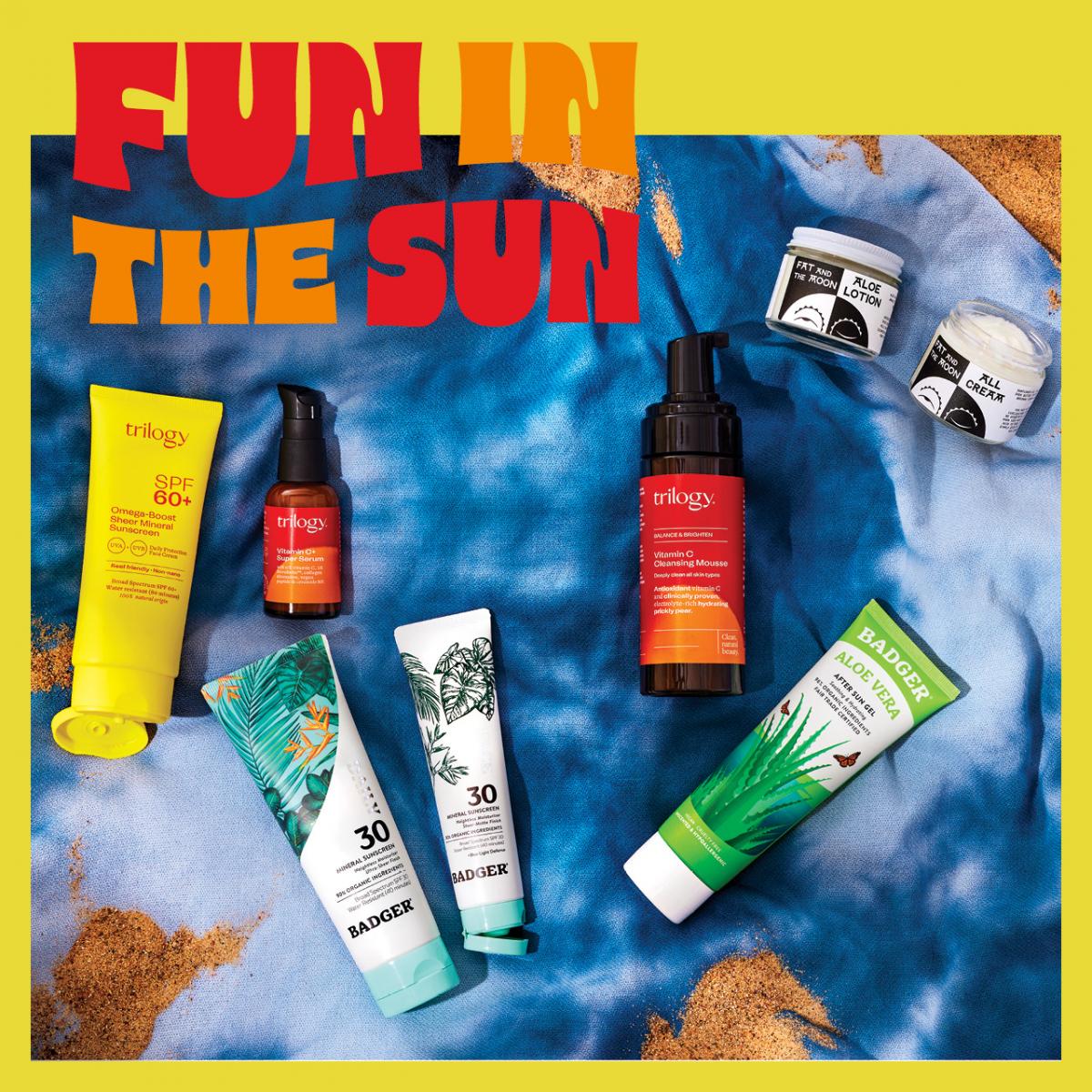 Variety of Healthy Living products for suncare and skincare on blue fabric with sand and text: Fun in the Sun