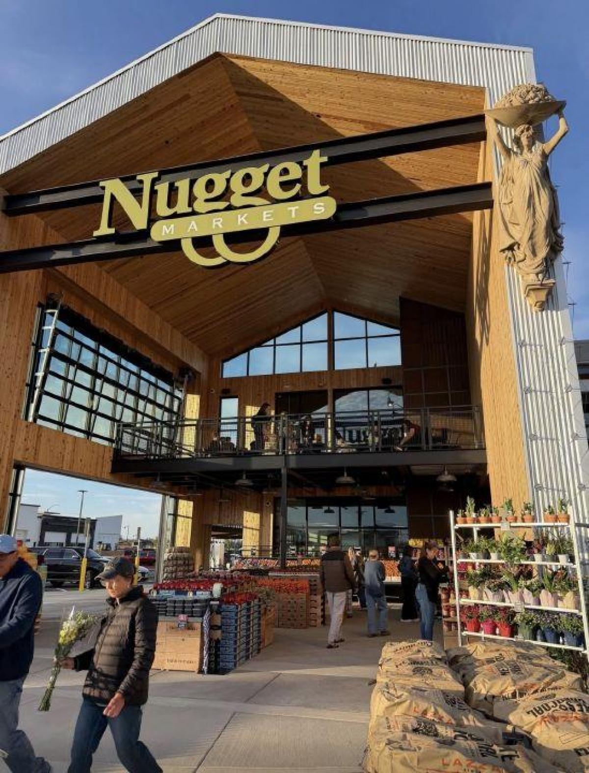 Exterior of the new Nugget Markets store in Rocklin on opening day, with customers entering under a wood-beam entrance and a stone goddess statue at right