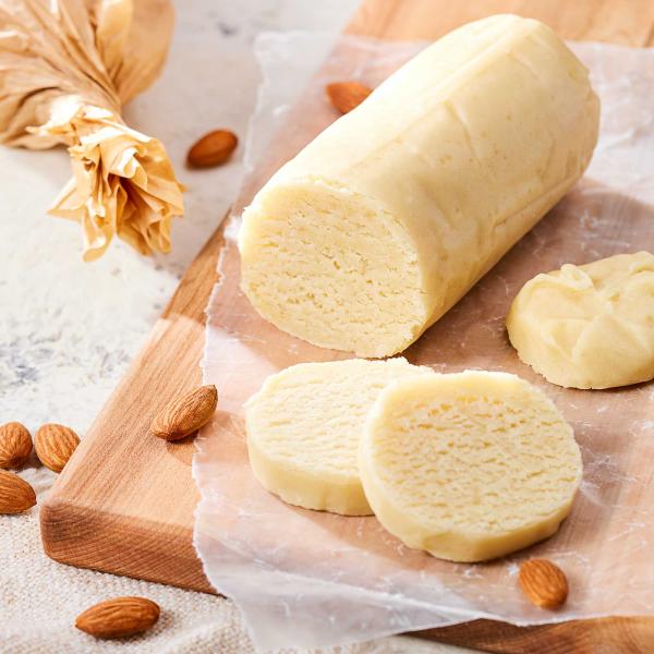 Marzipan log with slices cut on board with parchment paper and whole almonds on surface