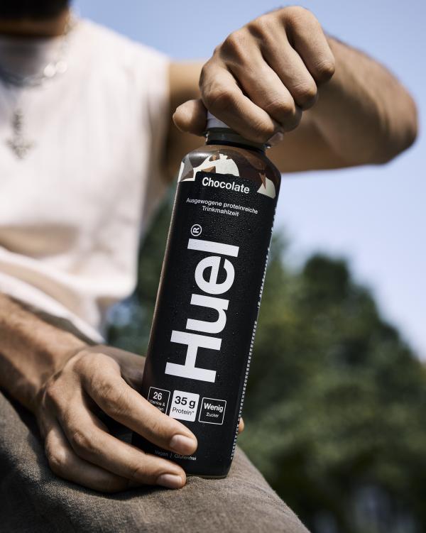 Two hands holding a bottle of Huel Chocolate Protein Drink outside