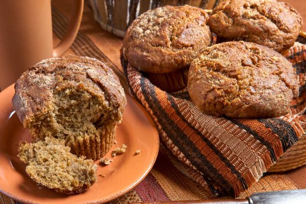 Basket of pumpkin muffins with one muffin on a plate broken into so you can see the inside crumb