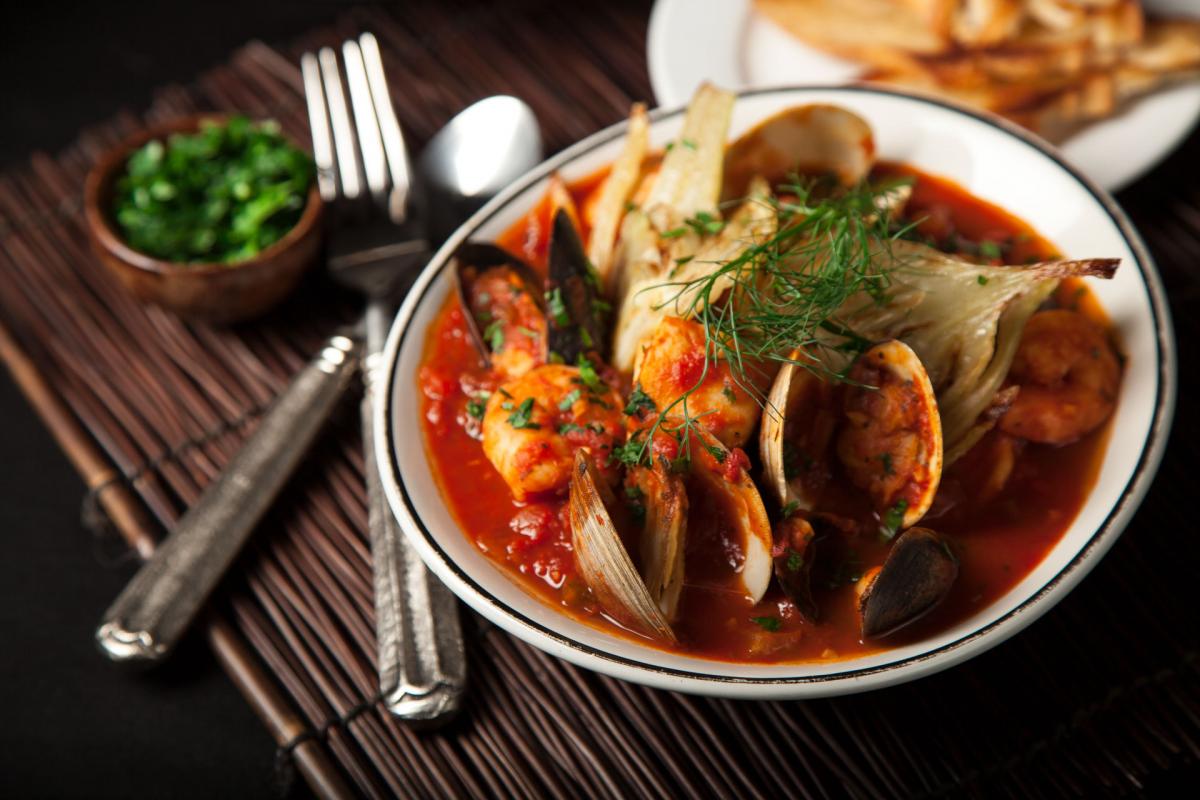 Seafood Stew in a bowl next to fork, spoon, and small bowl of herbs