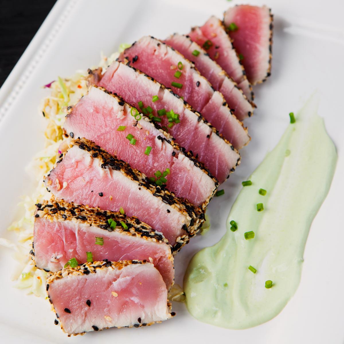 Sliced sesame crusted ahi tuna with wasabi cream on a white plate