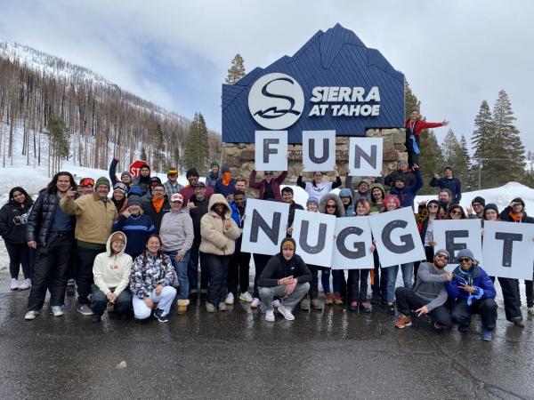nugget markets team on skiing and snowboarding trip with signs spelling "fun" and "nugget"