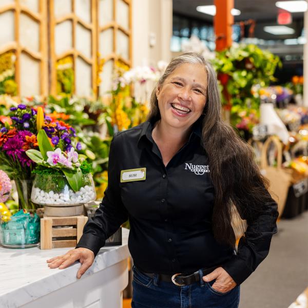 Floral Director Susi D. standing in Floral Department next to display of flowers, arrangements, and other plants