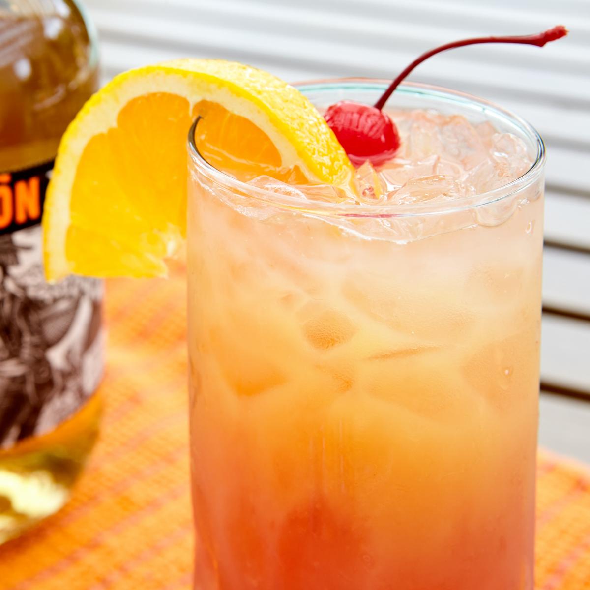 Tequila sunrise in a high ball glass on a beach blanket near a swimming pool