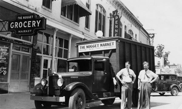 Black and white photo of Mack and Will Stille standing beside a truck labeled The Nugget Market outside The Nugget Grocery Market store