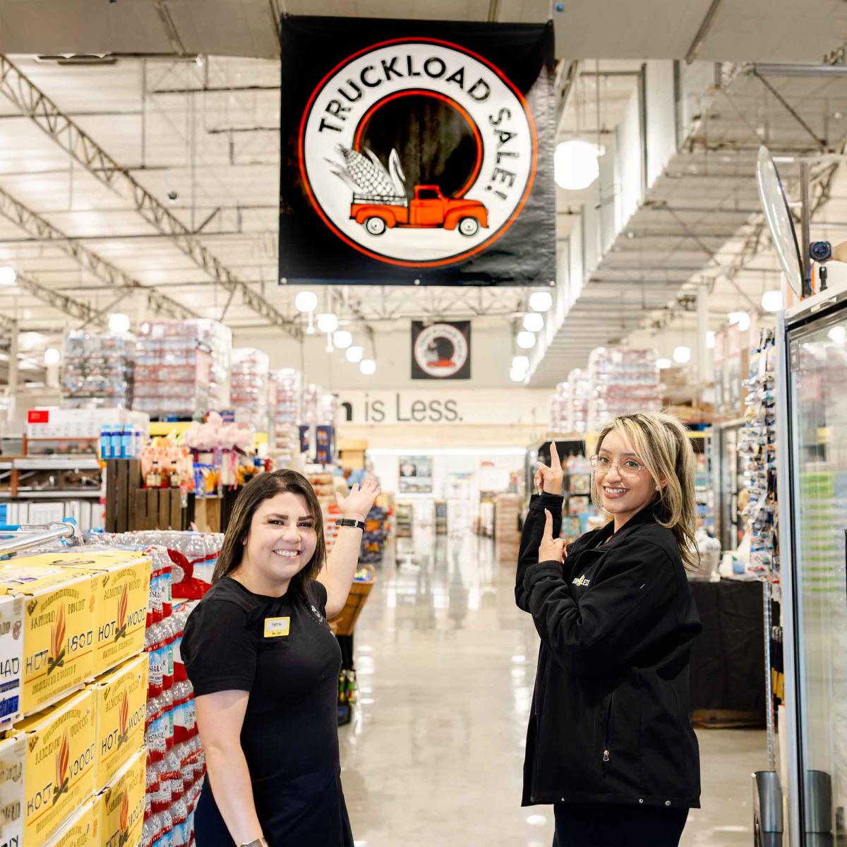 Two smiling associates inside Food 4 Less Woodland store pointing at Truckload Sale sign