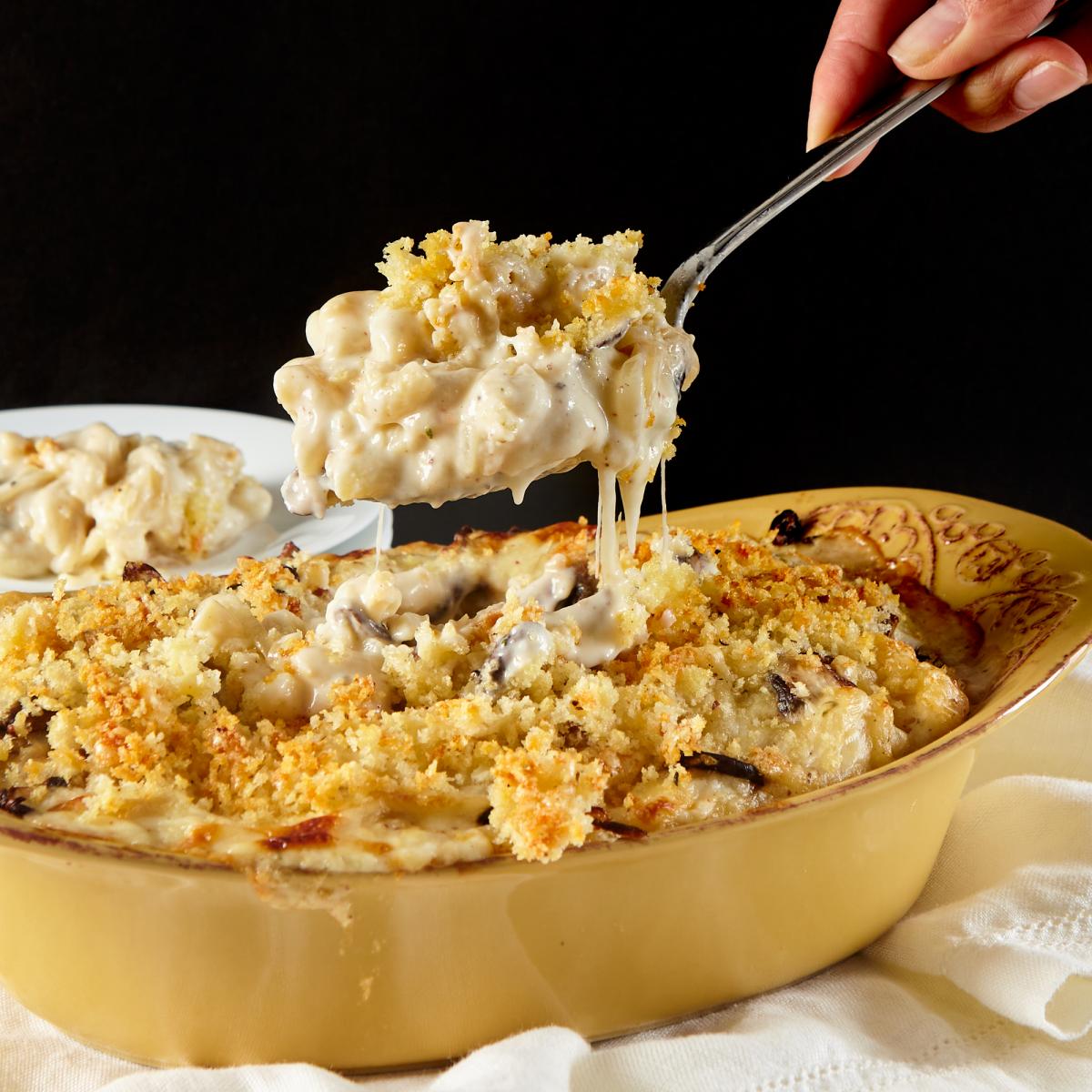 Hand holding spoon of Wild Mushroom Truffle Macaroni and Cheese over casserole dish