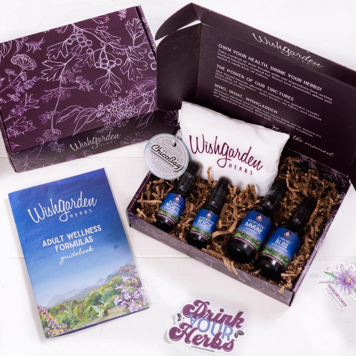 Closed purple box, open box of WishGarden Herbs bag and bottles, WishGarden Herbs Adult Wellness Formulas Guidebook, and "Drink Your Herbs" sticker