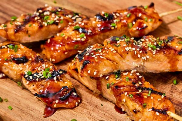 Yakitori salmon skewers on a wooden board with sesame seeds, green onions, and sauce